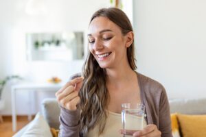 Mulher sorridente segura um copo de água e uma cápsula, reforçando o compromisso da Catarinense e Catarinense Nutrição, fonte de saúde do Brasil, em promover bem-estar e qualidade de vida.